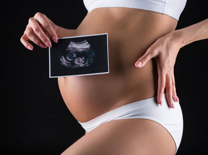 Mulher grávida segura imagem do exame de ultrassom de seu bebê